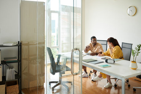 Coworkers sitting at table in meeting room discussing ideas for mobile app updateの写真素材