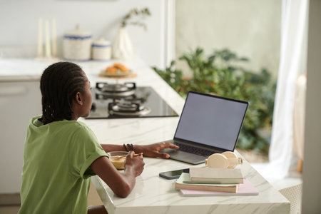 Black girl eating breakfast and watching entertaining video on laptopの写真素材