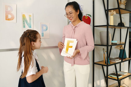 Teacher asking schoolgirl to name letters on cards in her hands