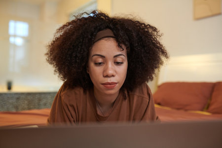 Woman lying on bed and reviewing code on laptop screenの写真素材