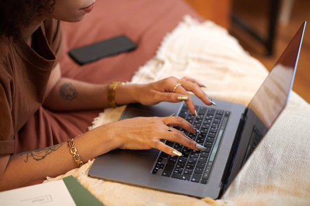 Hands of woman answering emails from customers on laptop when lying on bedの写真素材