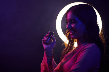 Smiling young woman smoking electronic cigarette in night clubの写真素材