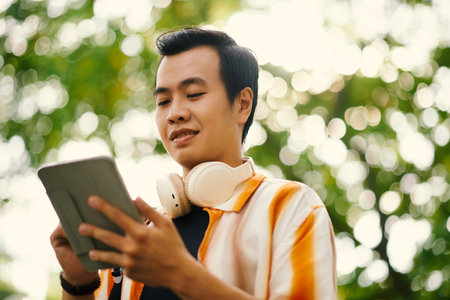 Young man with tablet looking at screen while communicating in video chat or watching online video...