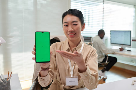 Portrait of smiling bank manager showing smartphone with green screen explaining how application...