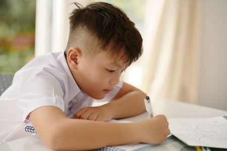 Vietnamese schoolboy writing in textbook at desk in class
