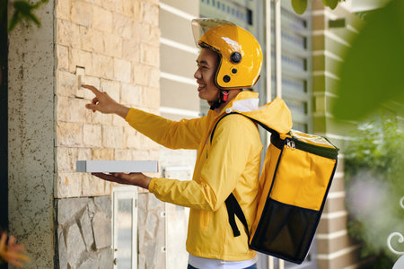 Smiling delivery man with pizza box ringing bell at door of customer