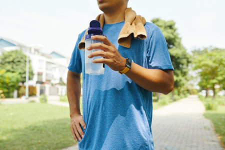 Cropped image of sweaty sportsman drinking water after working out outdoors