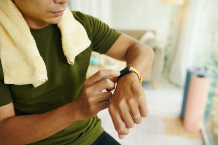 Cropped image of fit man checking pulse on his tracker after working out at home