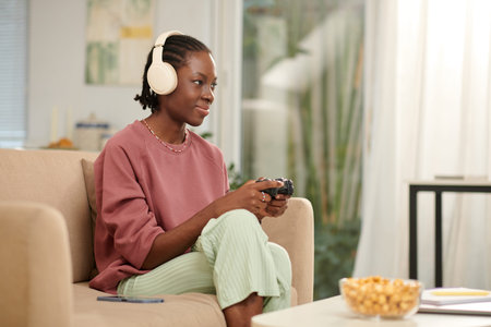 Smiling Black teenage girl playing videogame at home