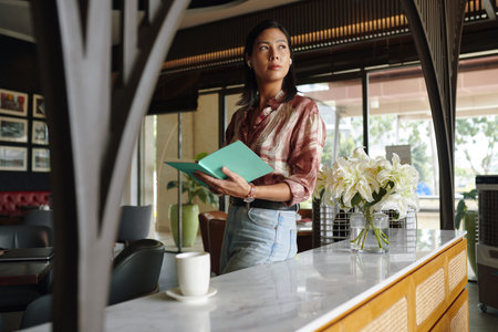 Pensive restaurant owner holding planner and looking awayの写真素材