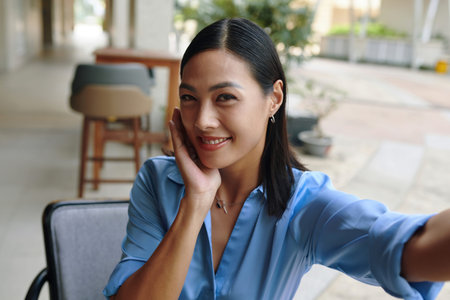 Smiling businesswoman in blue silk shirt taking selfie