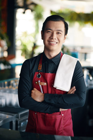 Smiling Vietnamese bartender with towel on shoulder working in restaurant