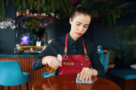 Waiter wiping restaurant tables with disinfecting sprayの写真素材