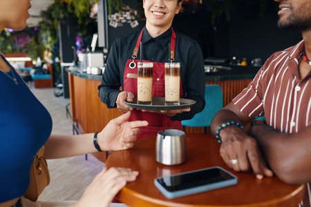 Waiter bringing iced coffee to couple at restaurant table