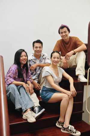 Smiling Vietnamese young people sitting on wooden steps at homeの写真素材