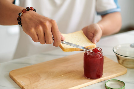 Closeup image of man spreading jam on piece of bread