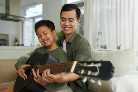 Smiling father teaching son to play chordsの写真素材