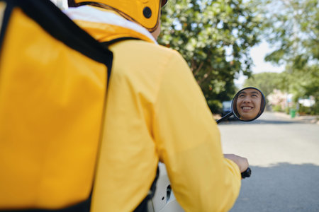 Smiling young man working as courier riding motorbike, view over shoulder