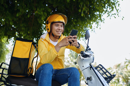 Portrait of smiling courier sitting on motorbike and reading text messages from managerの写真素材