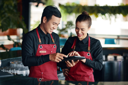 Restaurant manager teaching waiter how to use application when checking orders