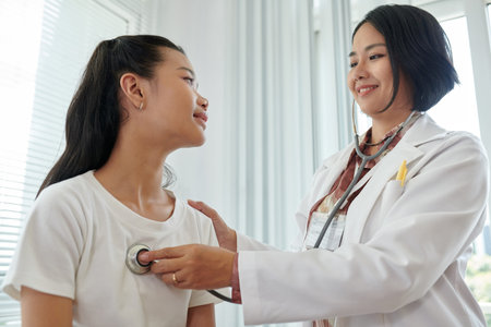 Smiling physician listening to breath of teenage girl with stethoscope