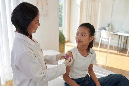 Smiling doctor sticking bandage on injection site on arm of teenage girl