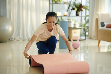 Woman rolling out yoga mat to exercise at homeの写真素材