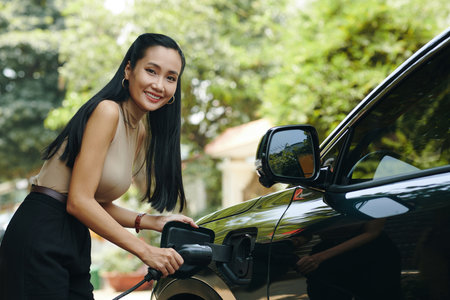 Portrait of smiling woman charging electric car after coming homeの写真素材