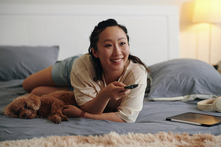 Happy woman relaxing on bed with her dog and watching movies