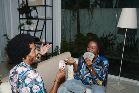 Cheerful Black couple enjoying playing cards at home after workの写真素材