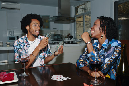 Black couple drinking wine and playing cards at homeの写真素材