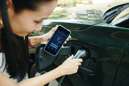 Cropped image of ev owner using smart charger app when charging electric car