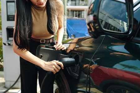 Cropped image of electric car owner inserting plug for charging