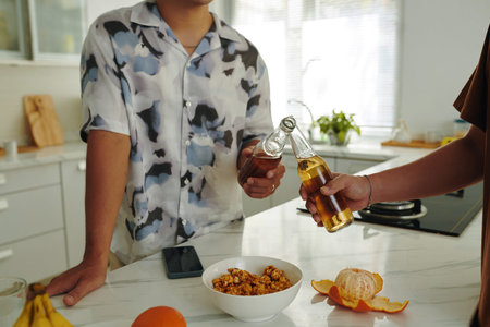 Two friends cheering with drinks and eating snacks in a modern kitchen, highlighting a moment of...