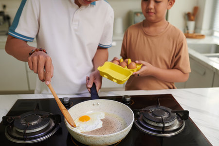Boy helping father to fry eggs for breakfastの写真素材