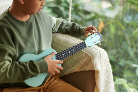 Cropped image of boy tuning ukulele before playing