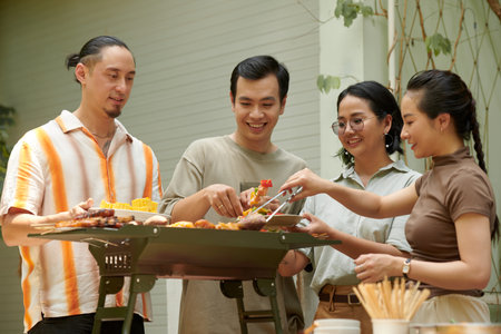 Group of friends hanging out together and cooking kebabsの写真素材