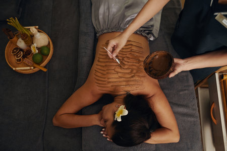Beautician applying chocolate peeling on back of woman, view from aboveの写真素材
