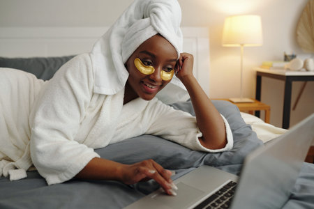 Resting in Bathrobe with Eye Patches Looking at Laptopの写真素材