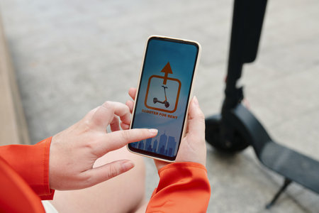 Using Smartphone App for Renting e-Scooter on City Streetの写真素材