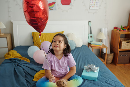 Girl Sitting With Balloon On Her Bedの写真素材