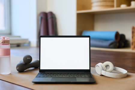Open laptop on mat surrounded by exercise equipment, including dumbbells, water bottle, and headphonesの写真素材