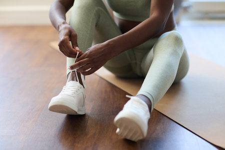 Close-up of a woman tying her sneakers before exercising on a yoga mat, wearing comfortable activewearの写真素材