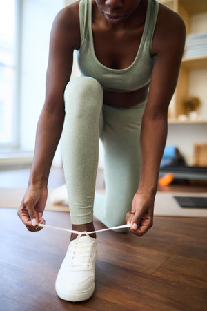 Close-up of woman tying shoelaces on white sports shoes, preparing for yoga session at homeの写真素材