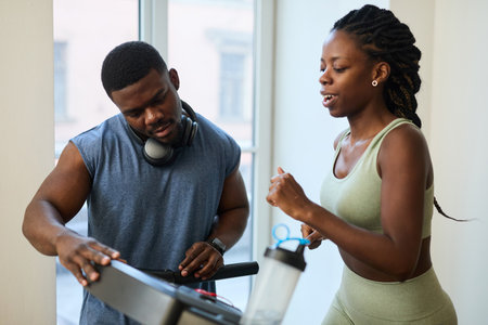 Two African American people exercising on treadmill in fitness center, engaging in conversation, and enjoying workoutの写真素材