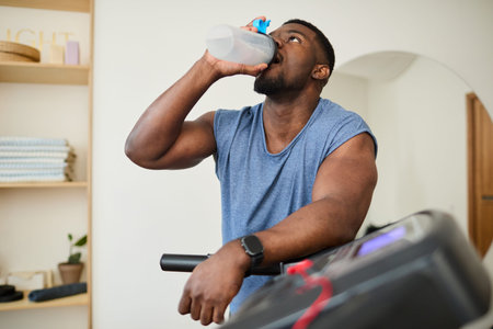 Man drinking water while taking break from treadmill workout in home gym setting
