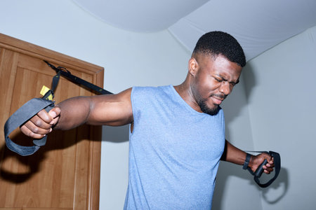 African American man using resistance bands for home workout, showing determination and focus in...