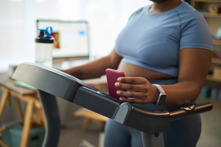 Black woman jogging on treadmill, wearing sporty clothing in a well-organized home gym environment....
