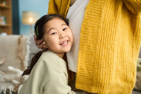 Smiling young girl holding parents hand in cozy living room, with various home decor in background, girl displaying joyful and happy expressionの写真素材