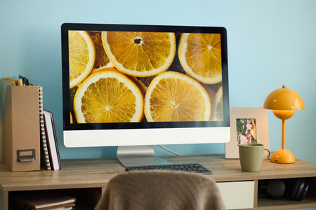 Desk setup with computer monitor displaying image of orange slices, alongside lamp and stationery items, creating a fresh, vibrant work environmentの写真素材